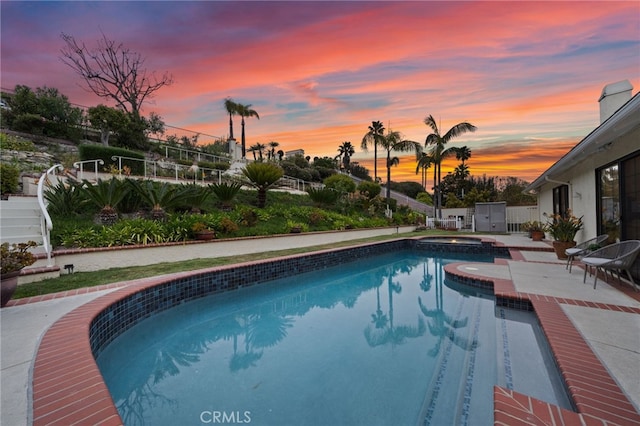 pool at dusk featuring fence, a pool with connected hot tub, and a patio area