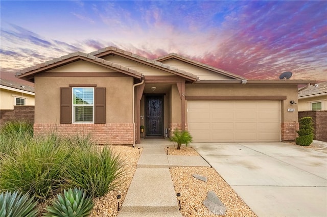 ranch-style house featuring stucco siding, concrete driveway, an attached garage, brick siding, and a tiled roof