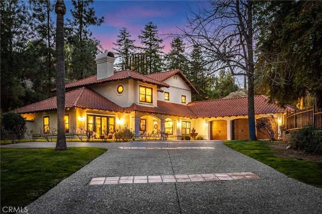 mediterranean / spanish-style home with a garage, a tiled roof, decorative driveway, a front lawn, and a chimney