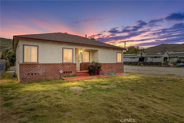 rear view of property featuring brick siding, stucco siding, a lawn, and fence