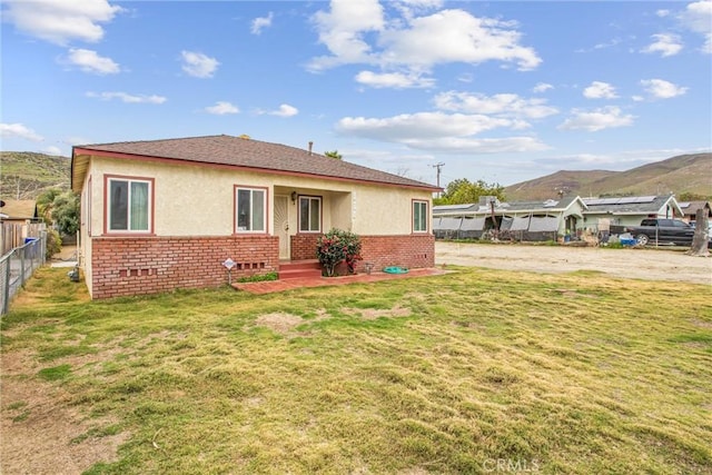 back of house featuring a yard, brick siding, stucco siding, and fence