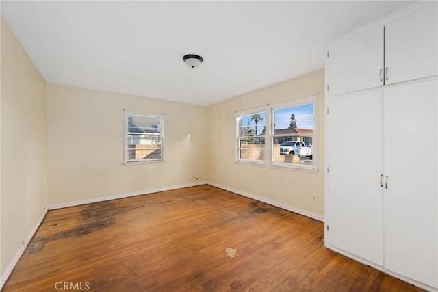 unfurnished bedroom with multiple windows, baseboards, and wood finished floors