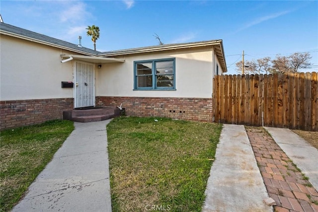 view of front facade with stucco siding, a front yard, fence, and brick siding