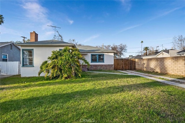 back of house with a yard, a chimney, fence, and stucco siding