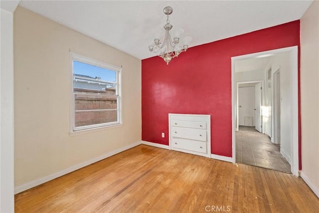 empty room with an inviting chandelier, baseboards, and wood finished floors