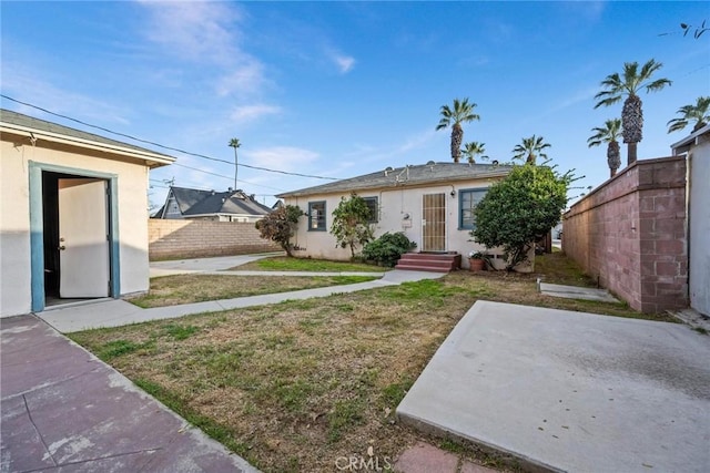 view of front of home featuring entry steps, an outdoor structure, fence, stucco siding, and a front yard