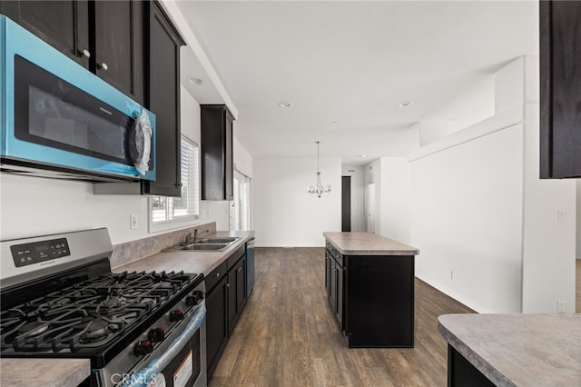 kitchen featuring dark cabinets, stainless steel appliances, dark wood-style flooring, a kitchen island, and a sink