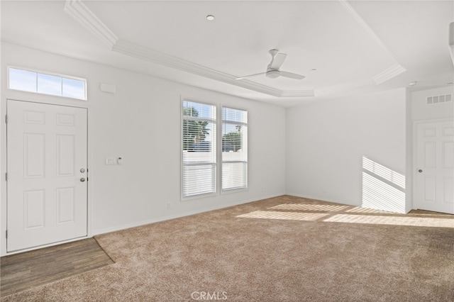 carpeted foyer entrance with crown molding, a raised ceiling, visible vents, ceiling fan, and baseboards