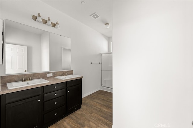 bathroom featuring double vanity, visible vents, a shower with door, wood finished floors, and a sink