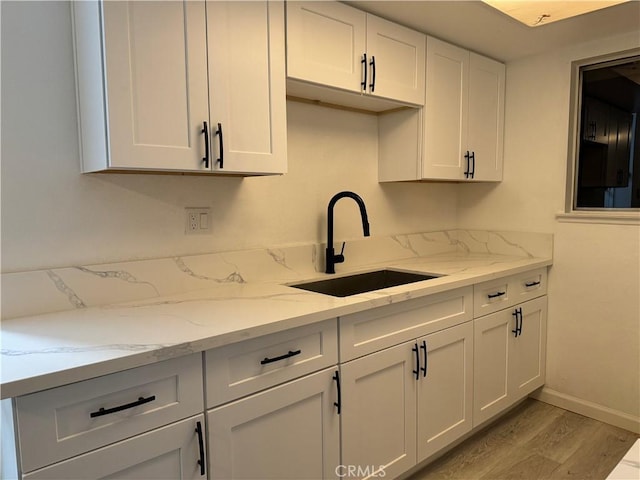 kitchen with light stone counters, light wood-style flooring, white cabinets, a sink, and baseboards