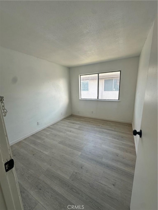 spare room with a textured ceiling, wood finished floors, and baseboards