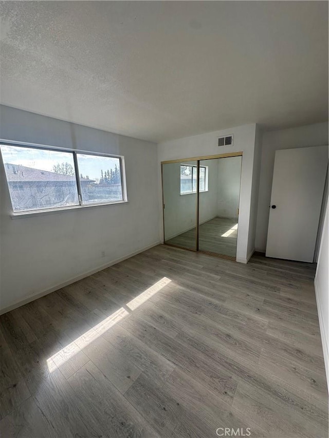 unfurnished bedroom featuring a closet, visible vents, a textured ceiling, and wood finished floors