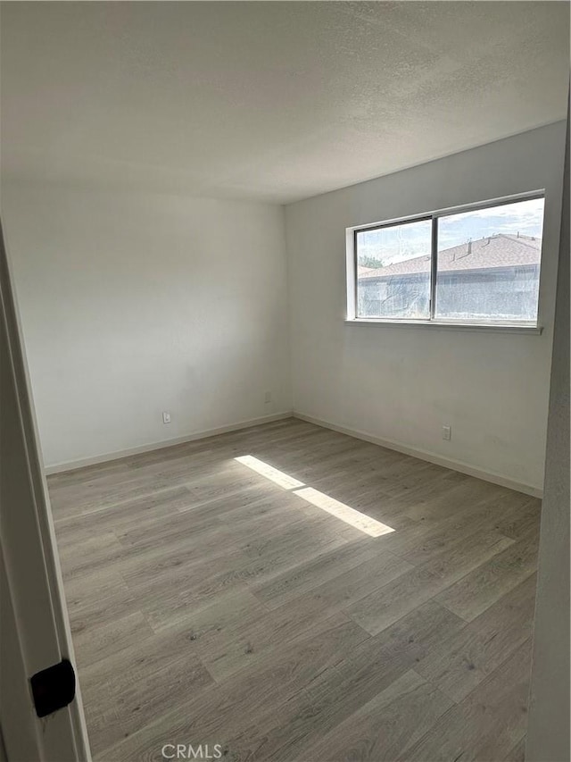 unfurnished room featuring a textured ceiling, baseboards, and wood finished floors