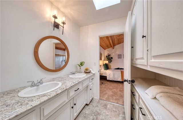 bathroom featuring vaulted ceiling with skylight, a sink, ensuite bathroom, and double vanity