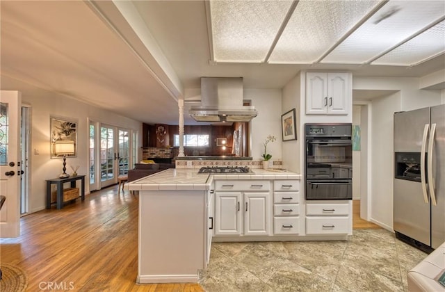 kitchen featuring tile countertops, a peninsula, appliances with stainless steel finishes, a warming drawer, and island exhaust hood