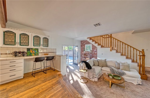 living area with light wood-style floors, built in desk, visible vents, and stairway