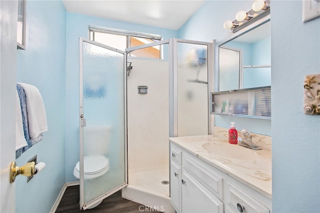 full bath with toilet, wood finished floors, vanity, baseboards, and a stall shower