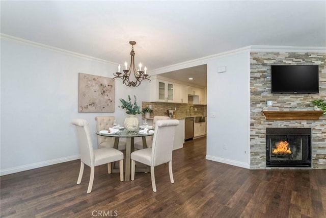 dining space with dark wood-style floors, crown molding, an inviting chandelier, a stone fireplace, and baseboards