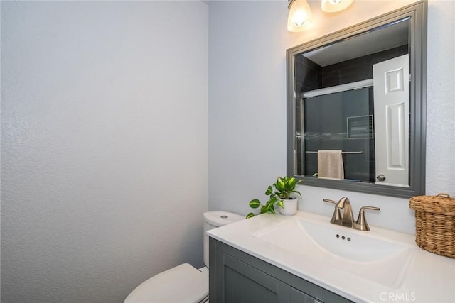 full bath featuring a shower with shower door, vanity, and toilet