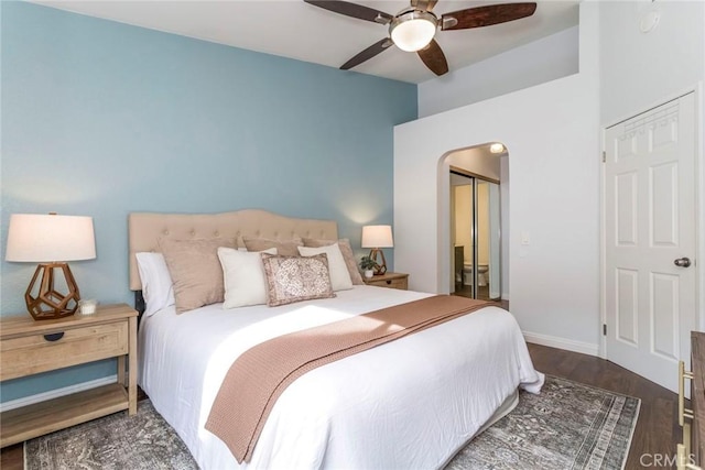 bedroom with arched walkways, wood finished floors, a ceiling fan, baseboards, and a closet