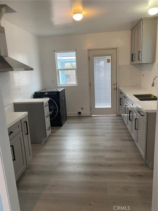 kitchen with washer / dryer, wall chimney exhaust hood, light wood-style flooring, and a sink