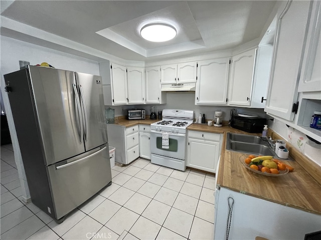 kitchen featuring freestanding refrigerator, white gas range, a tray ceiling, under cabinet range hood, and white cabinetry