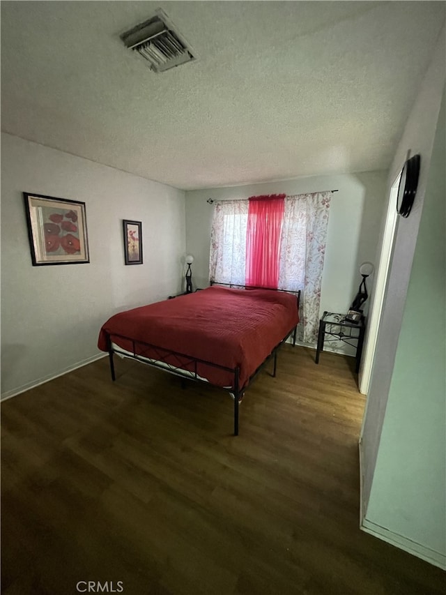 bedroom featuring a textured ceiling, visible vents, and wood finished floors