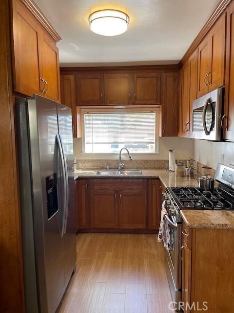 kitchen featuring appliances with stainless steel finishes, brown cabinets, a sink, and light stone countertops