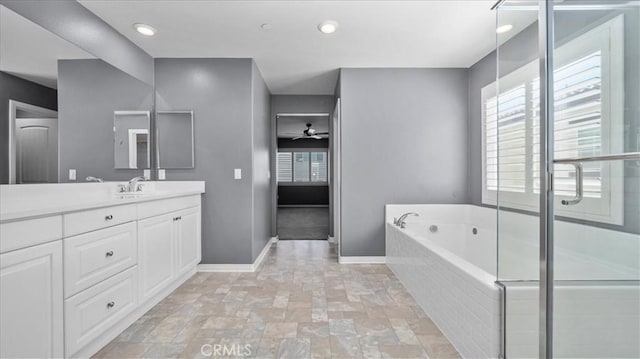 bathroom with a garden tub, stone finish flooring, ceiling fan, vanity, and baseboards