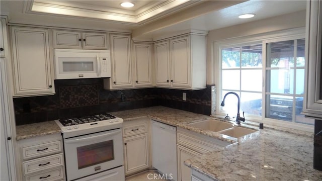 kitchen featuring light stone countertops, white appliances, backsplash, and a sink