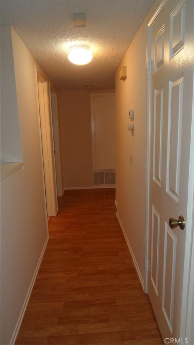 hall featuring a textured ceiling, wood finished floors, visible vents, and baseboards