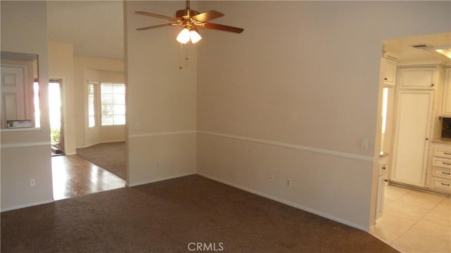 empty room with light carpet, ceiling fan, light tile patterned floors, and baseboards