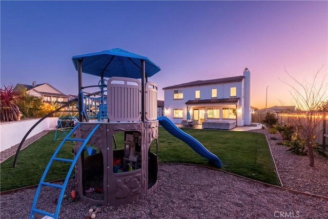 playground at dusk featuring a playground, a lawn, a fenced backyard, and a patio