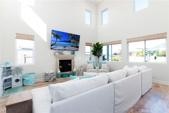 living room with a high ceiling, a fireplace, baseboards, and wood finished floors