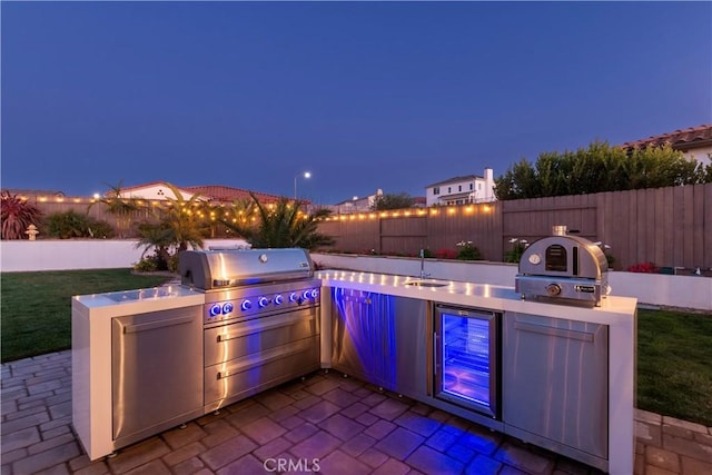 patio at twilight featuring a sink, area for grilling, fence, and a grill