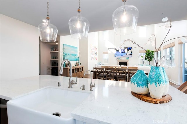 kitchen with light stone counters, a fireplace, a sink, open floor plan, and decorative light fixtures