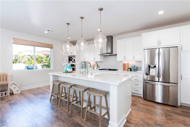 kitchen with a kitchen bar, light countertops, decorative backsplash, appliances with stainless steel finishes, and wall chimney exhaust hood