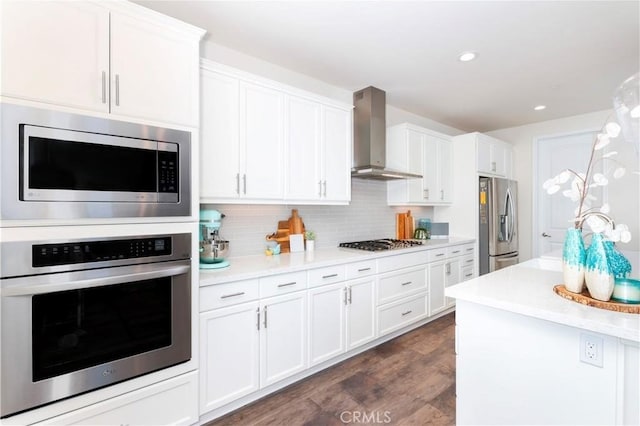 kitchen featuring white cabinetry, light countertops, appliances with stainless steel finishes, wall chimney range hood, and backsplash