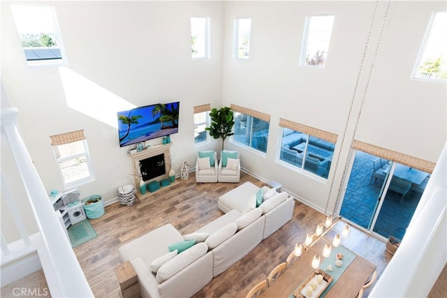 living area featuring a high ceiling, a fireplace, wood finished floors, and a healthy amount of sunlight