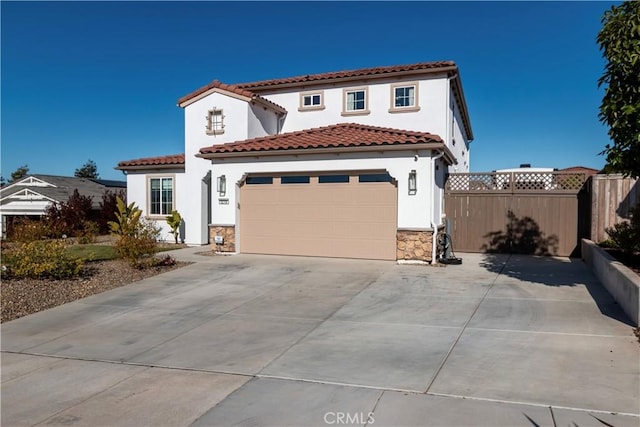 mediterranean / spanish-style home with stucco siding, fence, a garage, stone siding, and a tiled roof