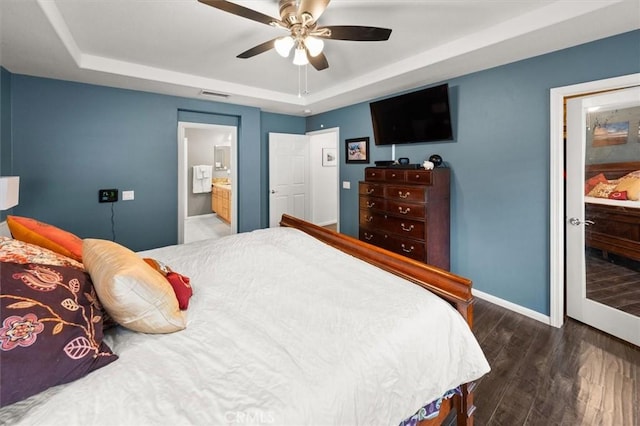 bedroom with a tray ceiling, visible vents, baseboards, and wood finished floors