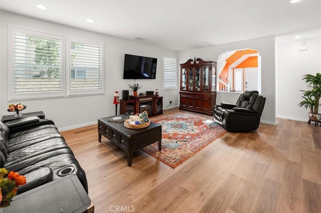 living room featuring arched walkways, light wood-type flooring, a wealth of natural light, and baseboards