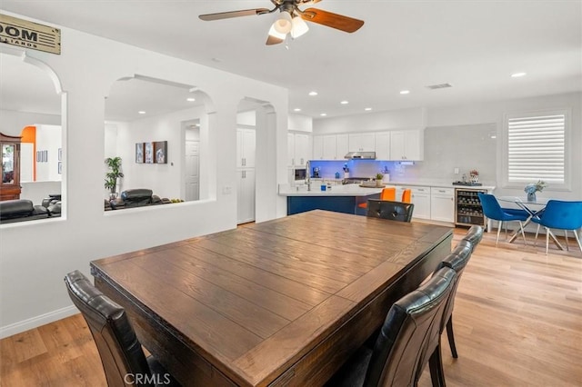 dining area with visible vents, arched walkways, wine cooler, a healthy amount of sunlight, and light wood-style floors