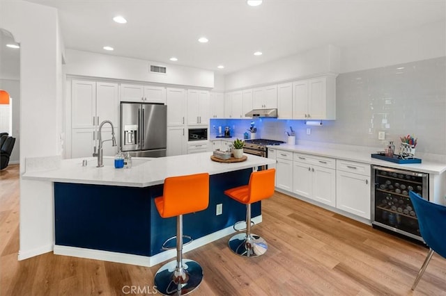 kitchen featuring wine cooler, arched walkways, stainless steel appliances, visible vents, and under cabinet range hood