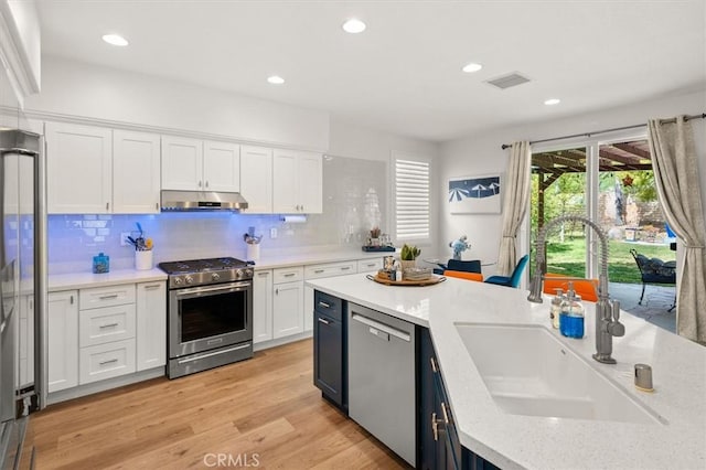 kitchen with stainless steel appliances, visible vents, white cabinetry, a sink, and under cabinet range hood