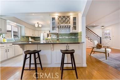 kitchen featuring light wood finished floors, a kitchen bar, glass insert cabinets, and decorative backsplash