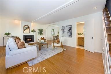 living room featuring a warm lit fireplace, stairway, and wood finished floors