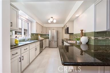 kitchen with stainless steel appliances, dark countertops, backsplash, a sink, and a peninsula