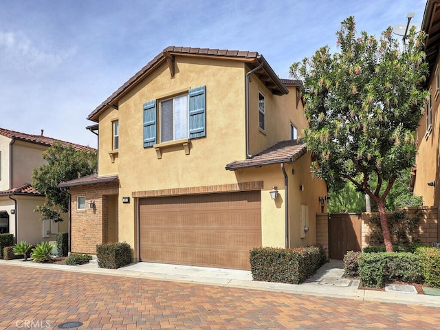 view of front facade featuring a garage, fence, a tiled roof, decorative driveway, and stucco siding