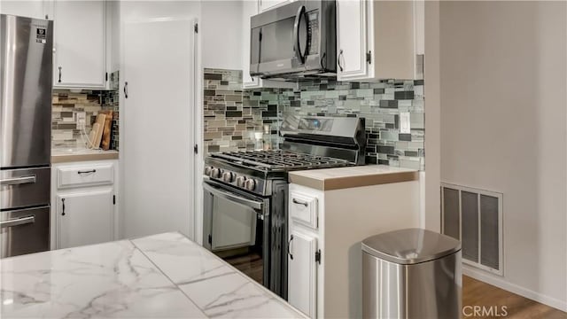 kitchen with white cabinets, visible vents, stainless steel appliances, and backsplash